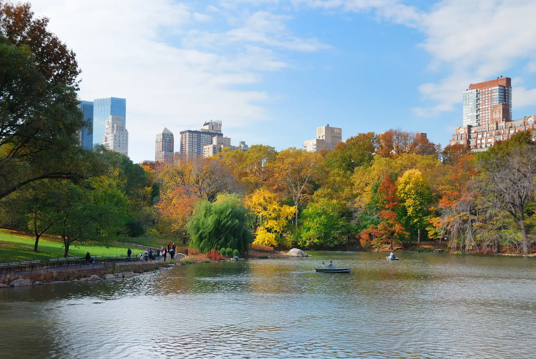 Central Park lake surrounded by colorful fall foliage with Manhattan buildings in the background.