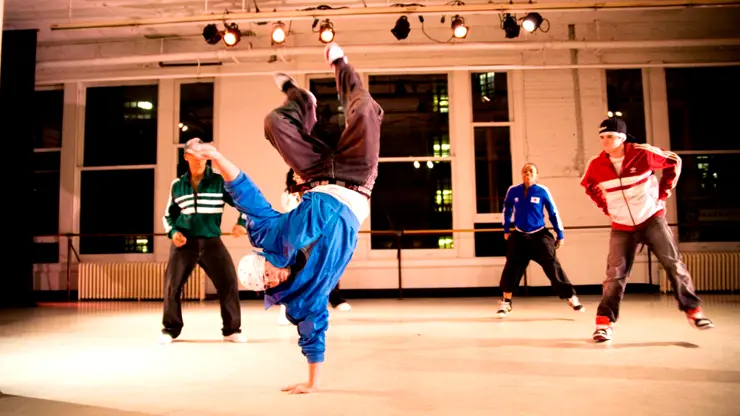 Students practicing hip-hop dance moves in a studio during an English plus dance program.