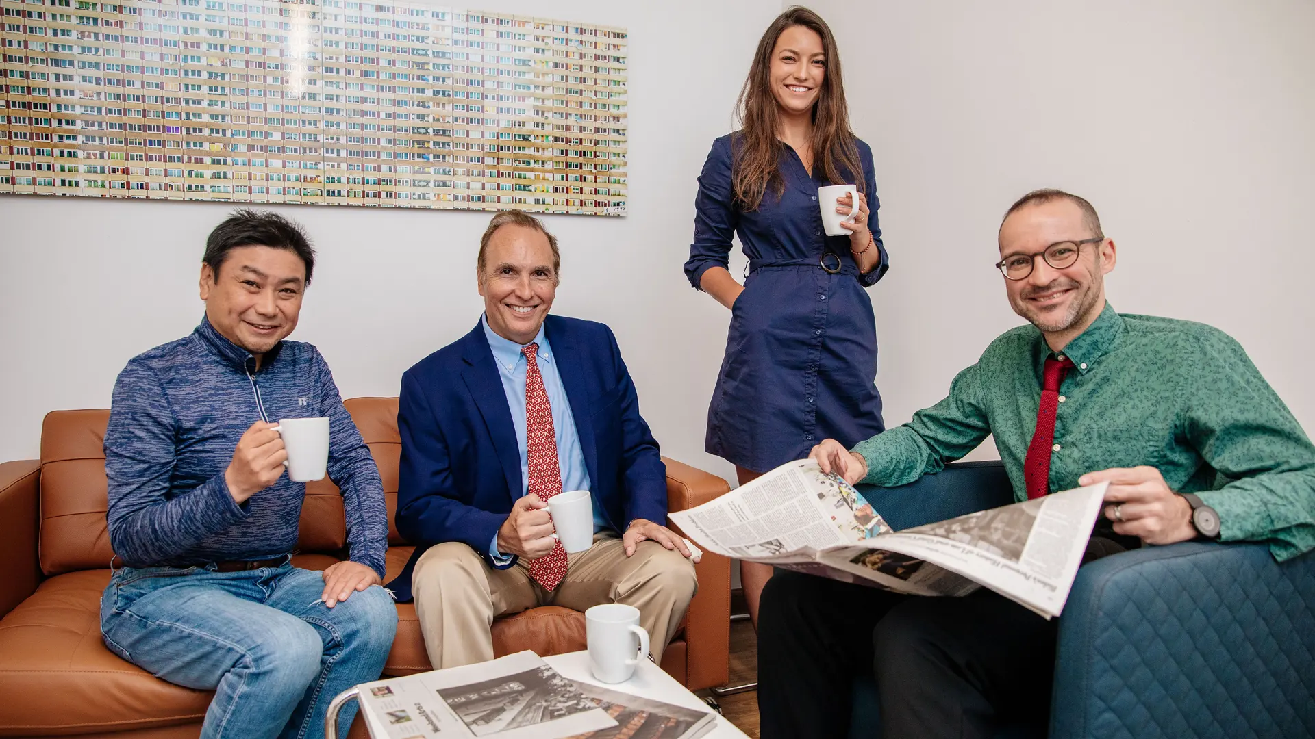 Professional group at Rennert English School enjoying a casual discussion over coffee and newspapers in a modern office setting