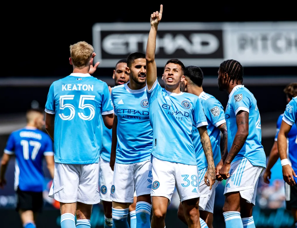 New York City FC team in blue uniforms on the field with the stadium in the background.